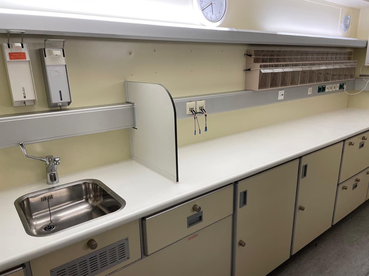 Clinical worktop with stainless steel sink, storage cupboards and wall service rail