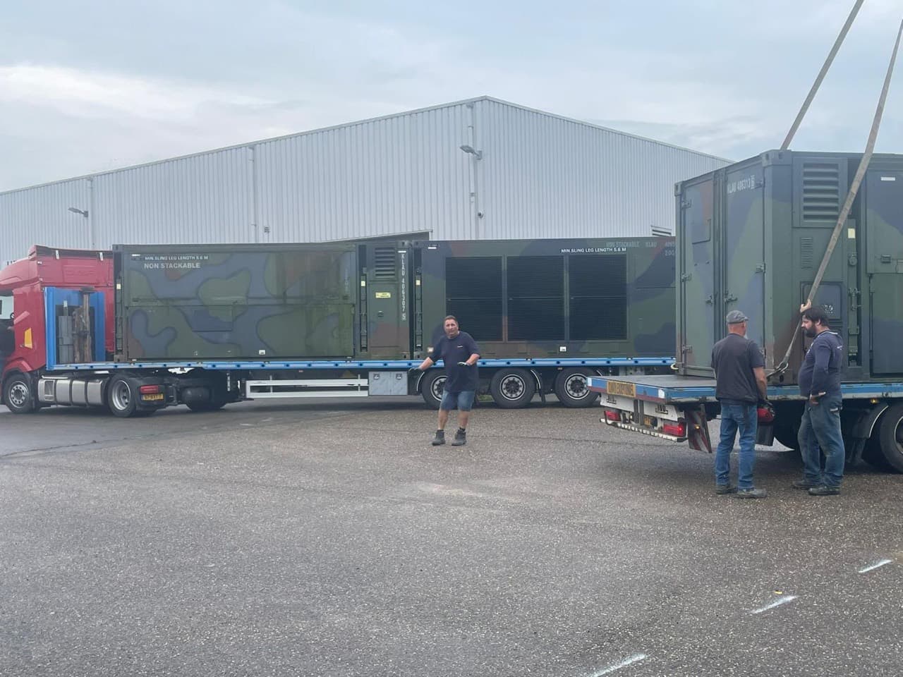 Hospital modules on trailers with workers and lifting straps during loading