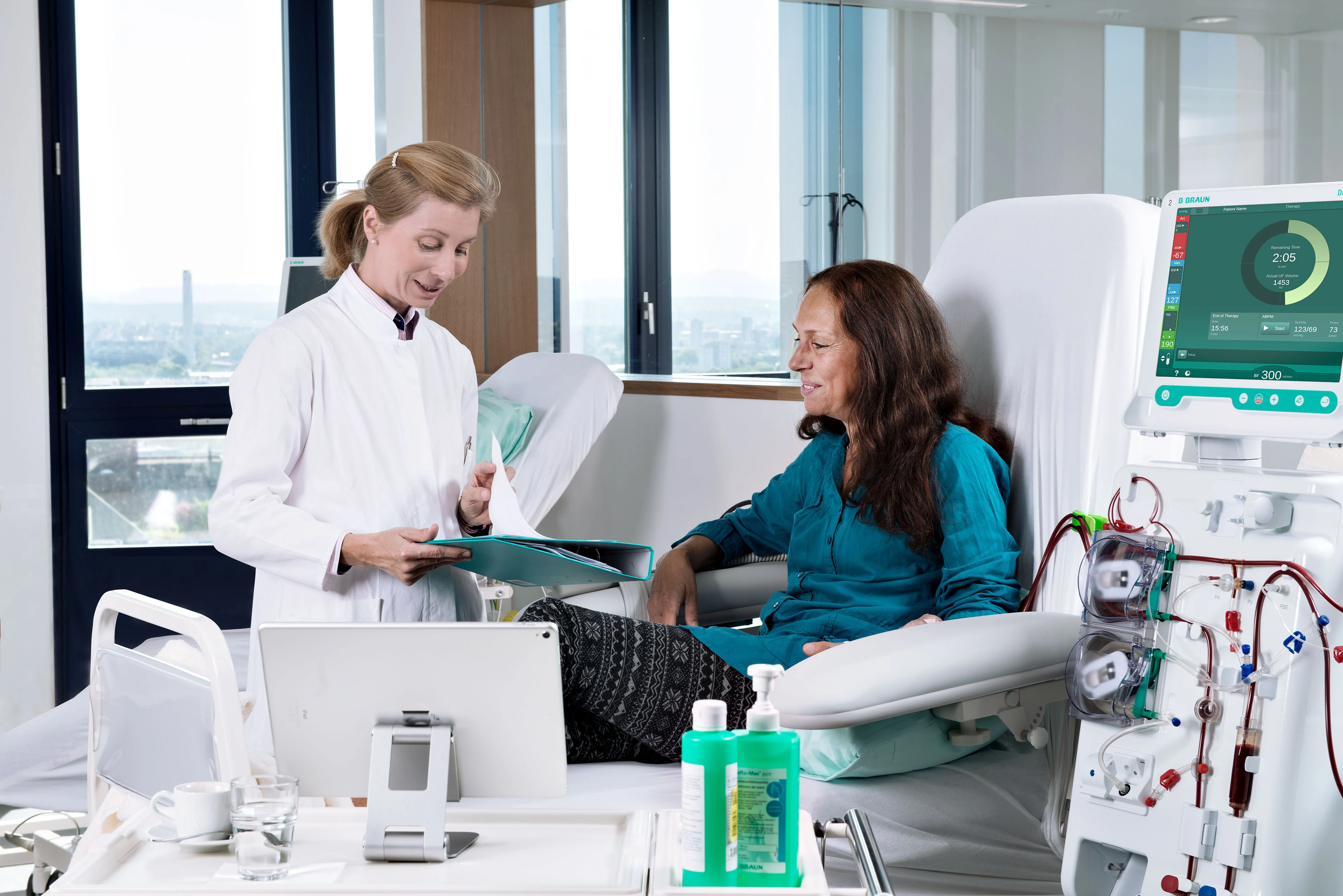 A physician reviews treatment with a patient beside a B. Braun dialysis system.