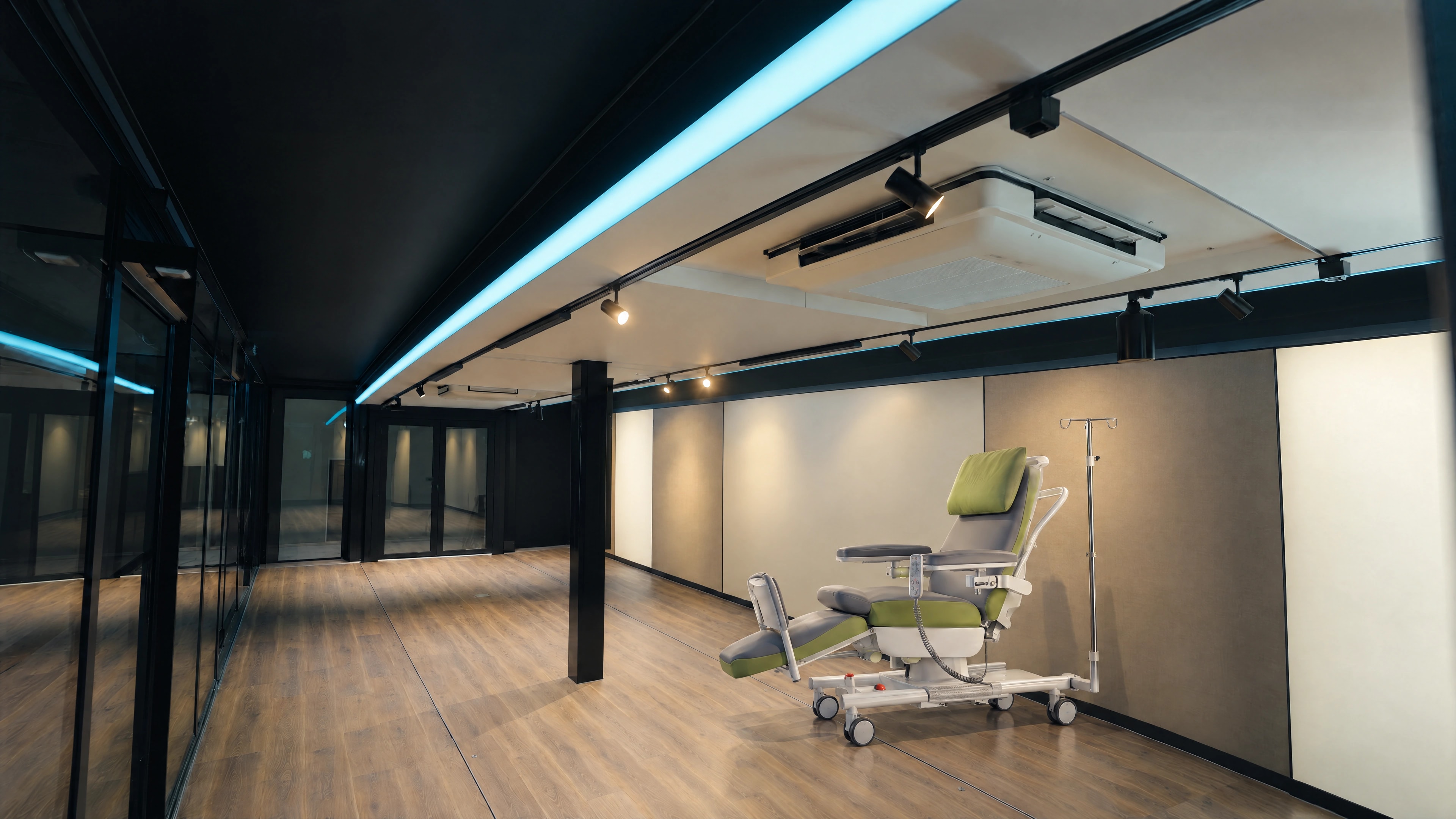 Illustrative single treatment-chair position beside a neutral wall, with a central black post, open floor and rear glazed opening in an expandable platform reference.