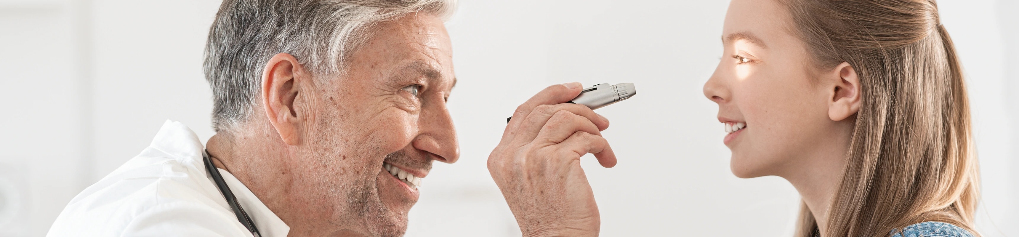 A clinician examines a patient with a HEINE handheld instrument.