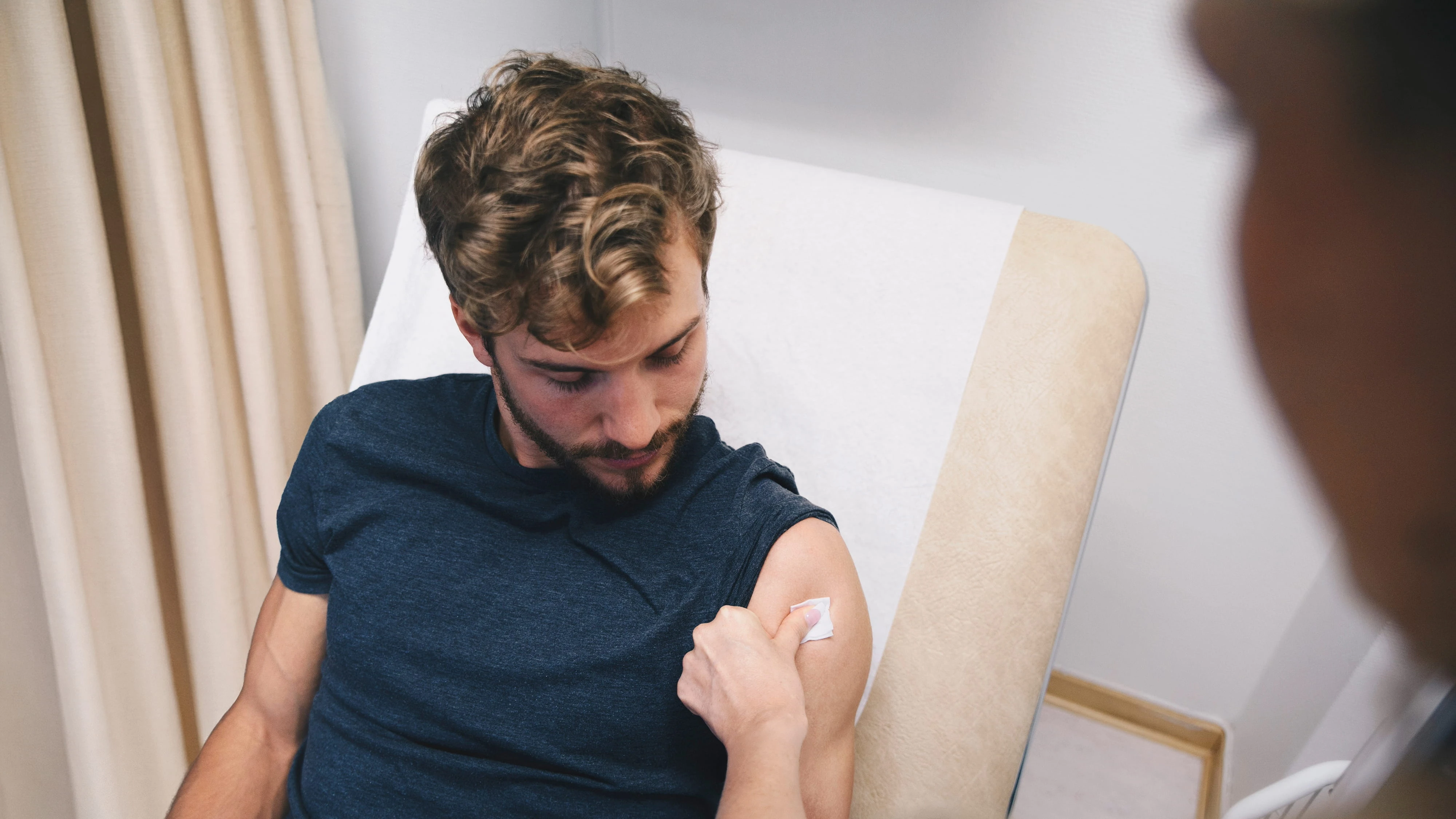 A patient holds cotton against his upper arm after a vaccination, with the clinician in the foreground.