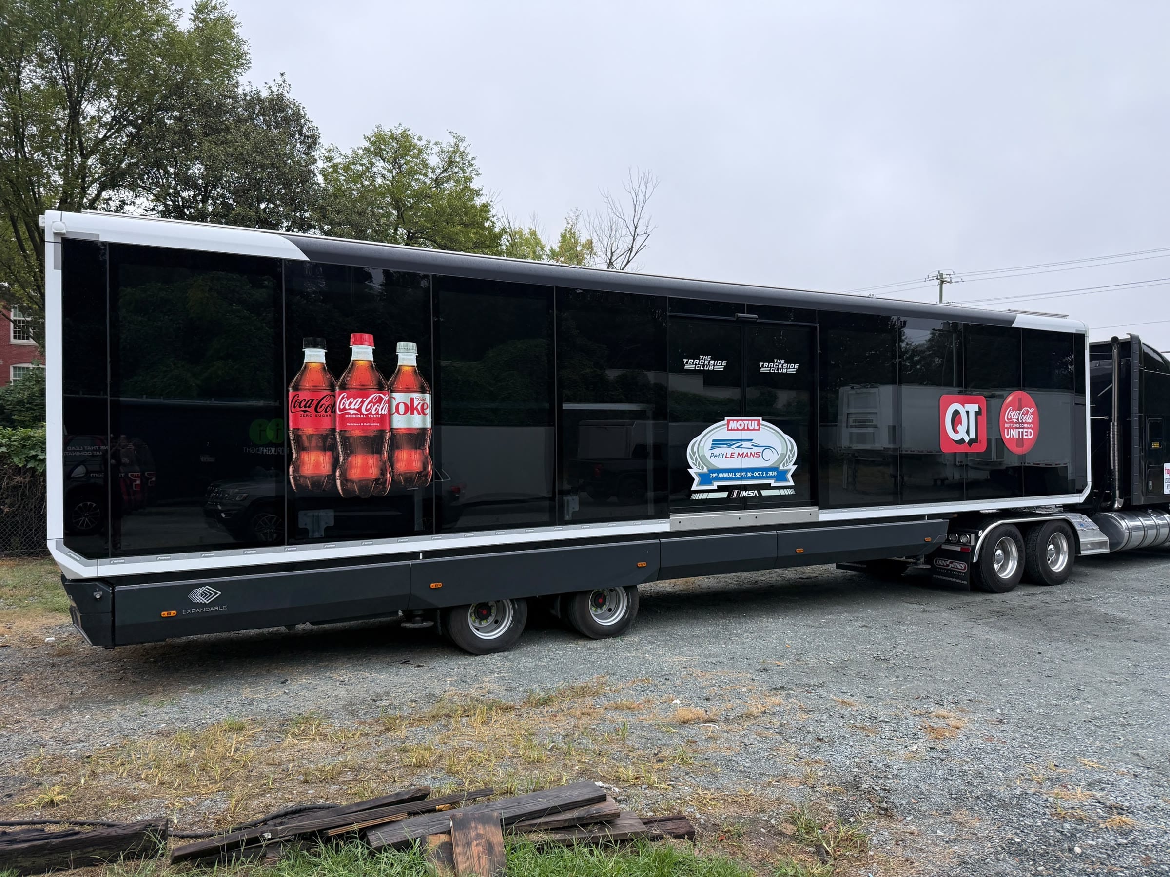 The expandable unit wrapped for the track, coupled to a tractor, with drinks graphics and event logos on its glass side